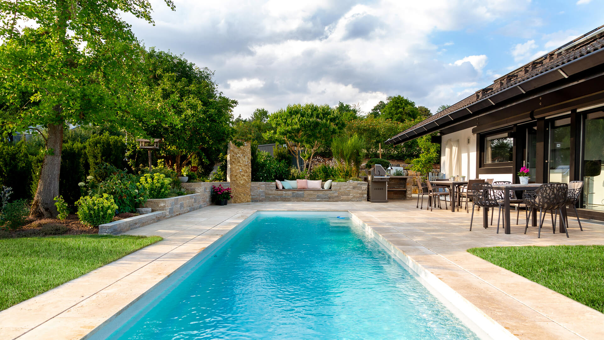 Haus mit schöner Terrasse neben einem Pool und grüner Bepflanzung
