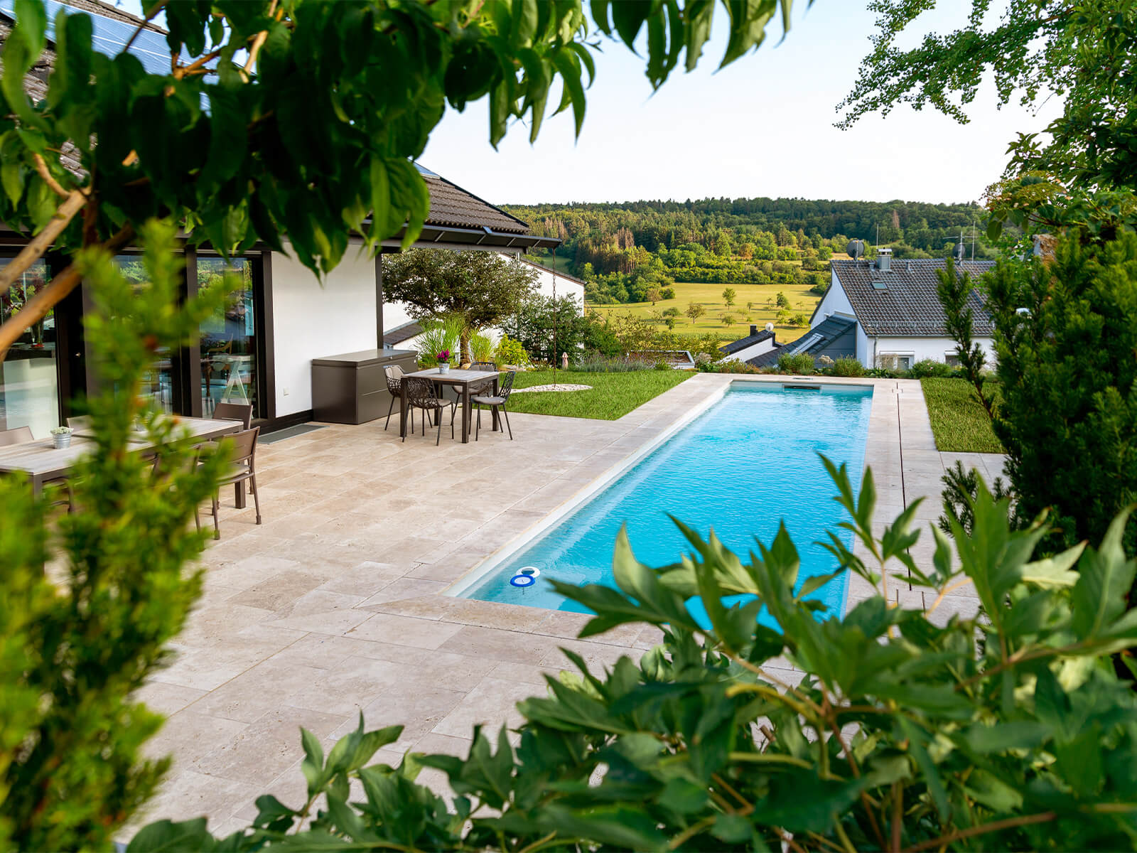 Blick durch Blätter auf einen Pool und einem dahinter liegendem Dorf